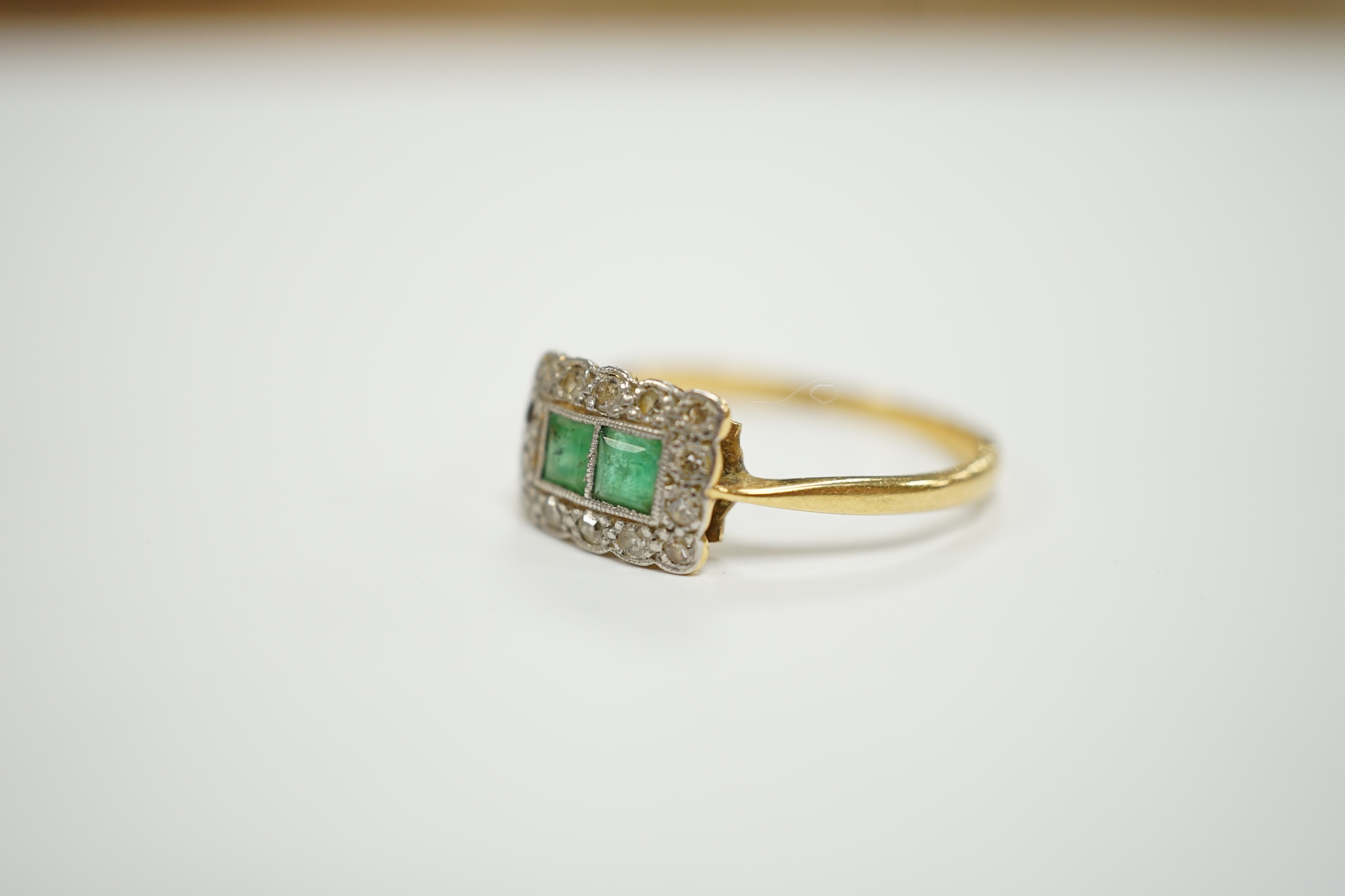 An 18ct, two stone emerald and diamond cluster set tablet ring, size M/N, gross weight 2.2 grams.